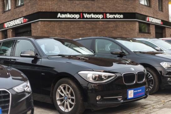 Gepersonaliseerde blauwe publiciteitsplaat en nummerplaathouder op een zwarte BMW in een showroom.