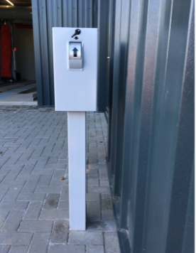 Vrijstaande sleutelzuil met sleutelkast en slot, geplaatst buiten aan bedrijfsgebouw.
